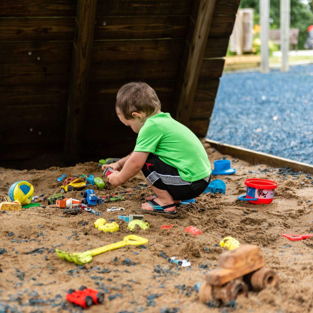 A Child at Coyote Hill's Harrisburg, MO, Foster Care Community plays in a sandbox, surrounded by colorful toys